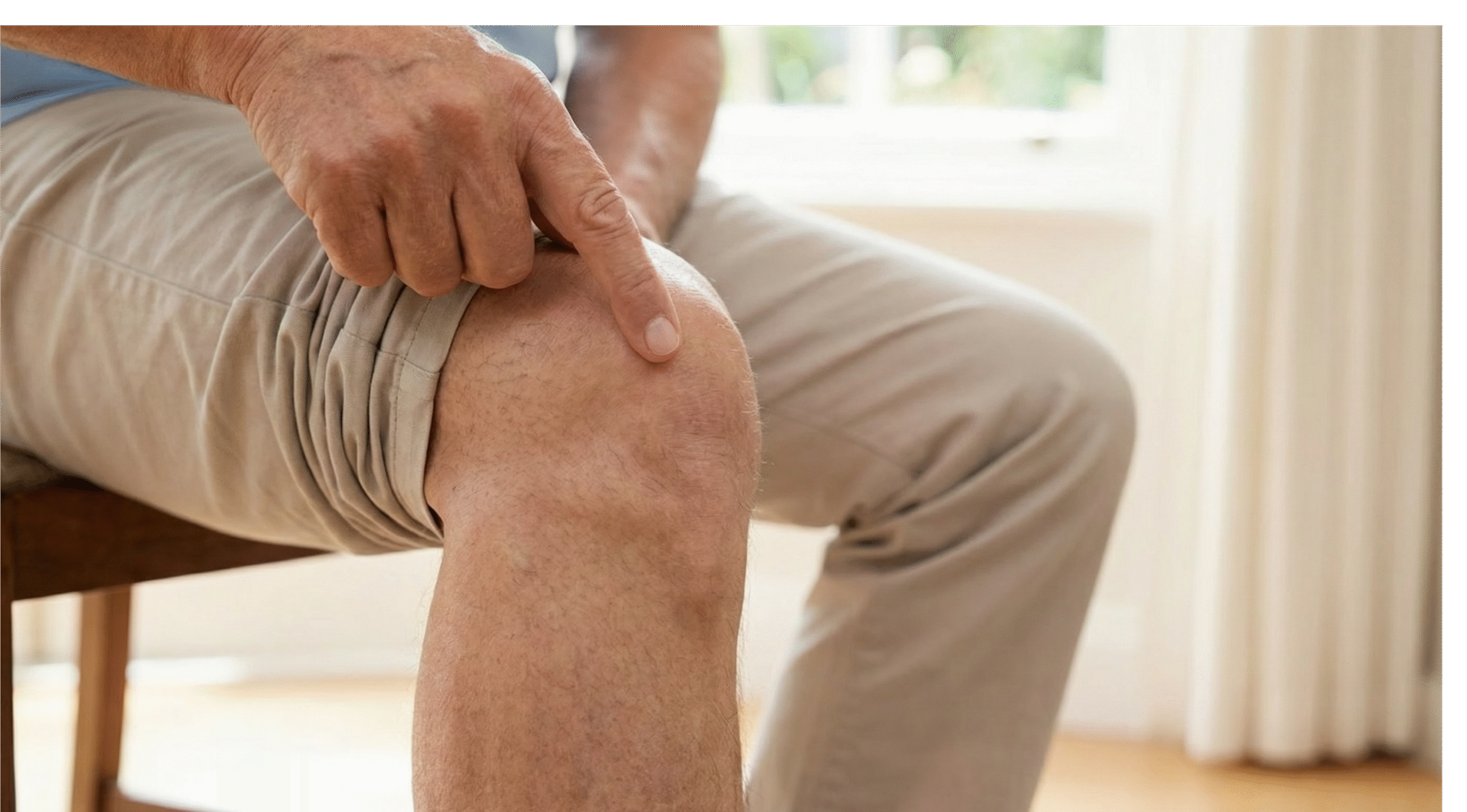 Plan rapproché sur le genou d'une personne senior assise. Elle pointe son index exactement sur la zone située sous la rotule (le tendon rotulien), illustrant la localisation précise de la douleur caractéristique de la tendinite par rapport à l'arthrose.